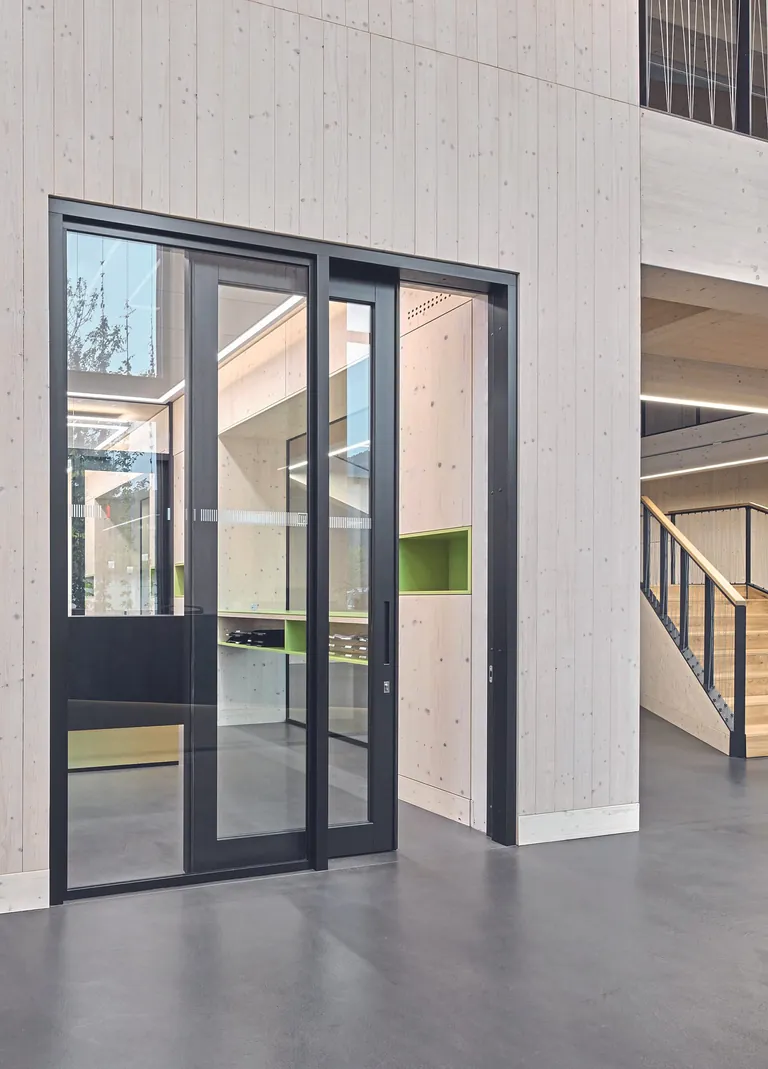 Zwei Schiebet&uuml;ren zu den B&uuml;ros im Erdgeschoss erm&ouml;glichen es, sich von Ger&auml;uschen im Atrium abzuschirmen.