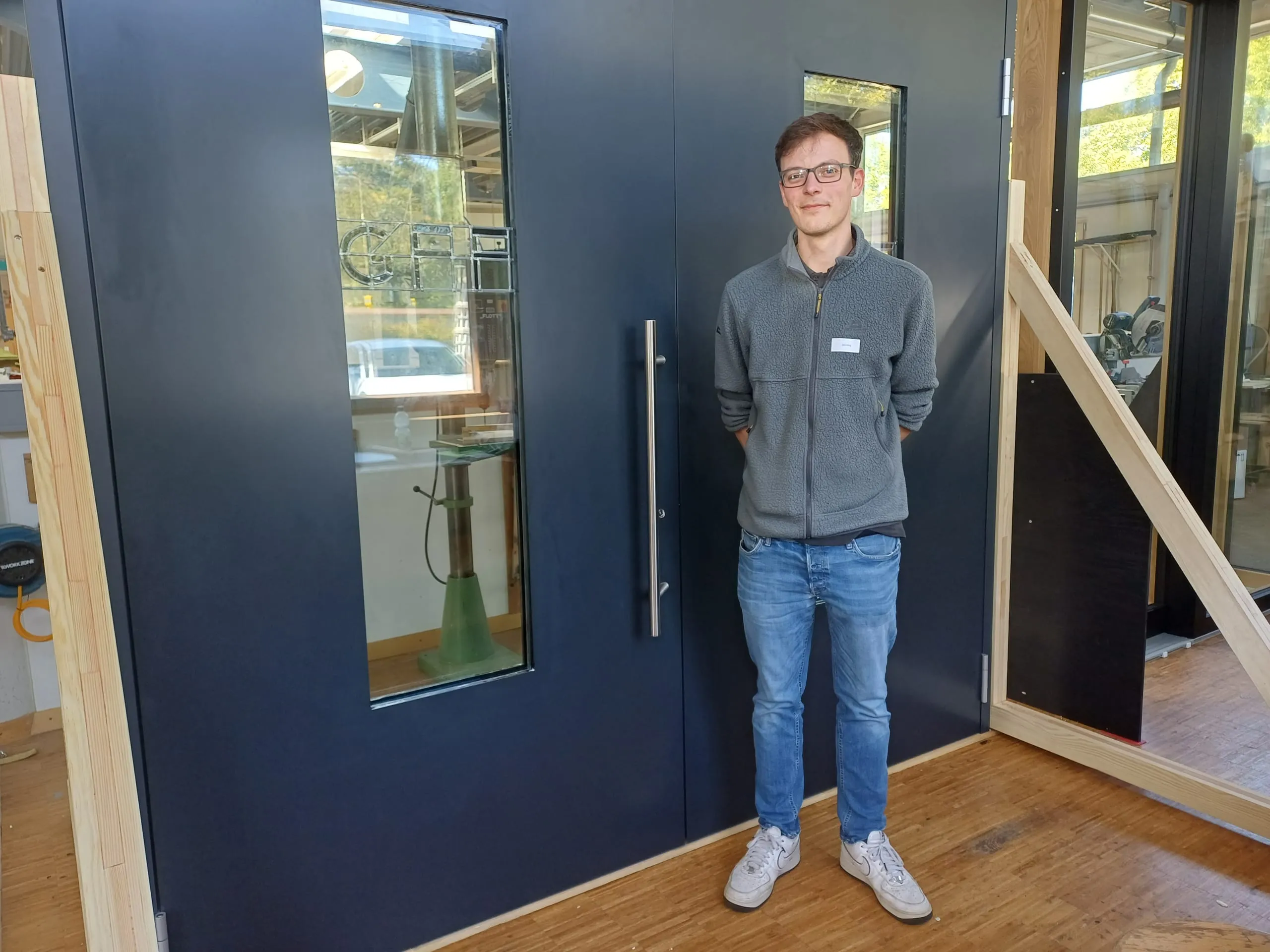 Am 18. September 2025 war es wieder soweit. Der nächste Vollzeit-Meisterkurs (MK 34) der Fachschule für Glas-, Fenster- und Fassadenbau in Karlsruhe präsentierte seine Meisterstücke und schloss damit die letzte Prüfung der Weiterbildung ab. Hier zu sehen: John König von Fenster Braun vor seiner maßgeschneiderten Aluminium-Stulptür ohne Mittelpfosten. Highlight der großformatigen, doppelflügeligen Tür ist eine Bleiverglasung mit dem Schriftzug "GFF", also die Abkürzung der Karlsruher Fachschule. So kommt das Meisterstück von König in der Schule selbst zum Einsatz und dient bald als Eingang zu einer der Werkstätten.