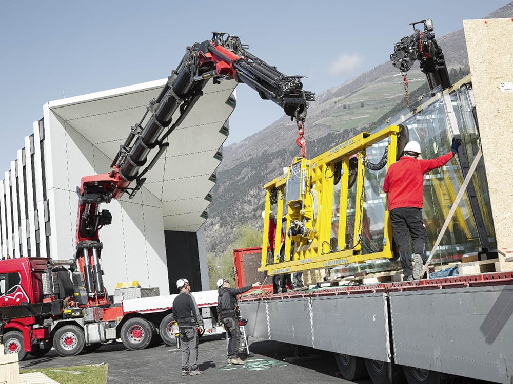 Ein weiteres Projekt von Heavydrive war die Verglasung am neuen Hauptsitz des Südtiroler Türen-, Fenster-, Fassaden- und Sonnensystemherstellers BSV. Das Firmengebäude in Schlanders (Italien) erstreckt sich über 120 Meter Länge und läuft spitz zu. Die Montage der 10,7 Meter hohen Sägezahn-Fassadenelemente wollte der Kunde ursprünglich mit einer einzigen Sauganlage realisieren, weil die Heavydrive Anlagen flexibel an die Scheibengröße anpassbar sind. Da die Finnglasscheiben und die breiten Glaselemente jedoch im Wechsel installiert werden mussten und der Umbau nach jeder Montage Zeit kostet, wurden letztlich zwei Sauganlagen eingesetzt: Die VSG 3500 KMH mit einer Spannweite von 8,5 Metern montierte die 2,3 Meter breiten und 2,8 Tonnen schweren Scheiben und die VSG 1000 KL9-4 die schmalen Fassadenelemente mit 0,57 Metern Breite und 750 Kilo Gewicht.