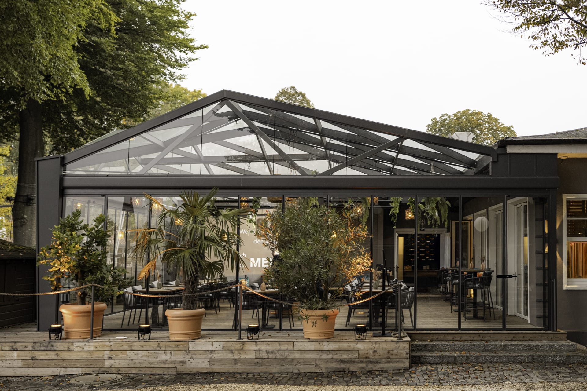 Unmittelbar am Ufer des Ammersees in Stegen befindet sich das Restaurant Fischer. Damit die rund 120 Sitzplätze auf der Terrasse künftig unabhängig von Wind und Wetter genutzt werden können, wurde das bestehende Satteldach mit filigraner Glasfachwerkstruktur auf zwei Seiten um eine flexible, senkrechte Verglasung ergänzt. Zum Einsatz kam dafür das Schiebe-Dreh-System Proline T von Solarlux.